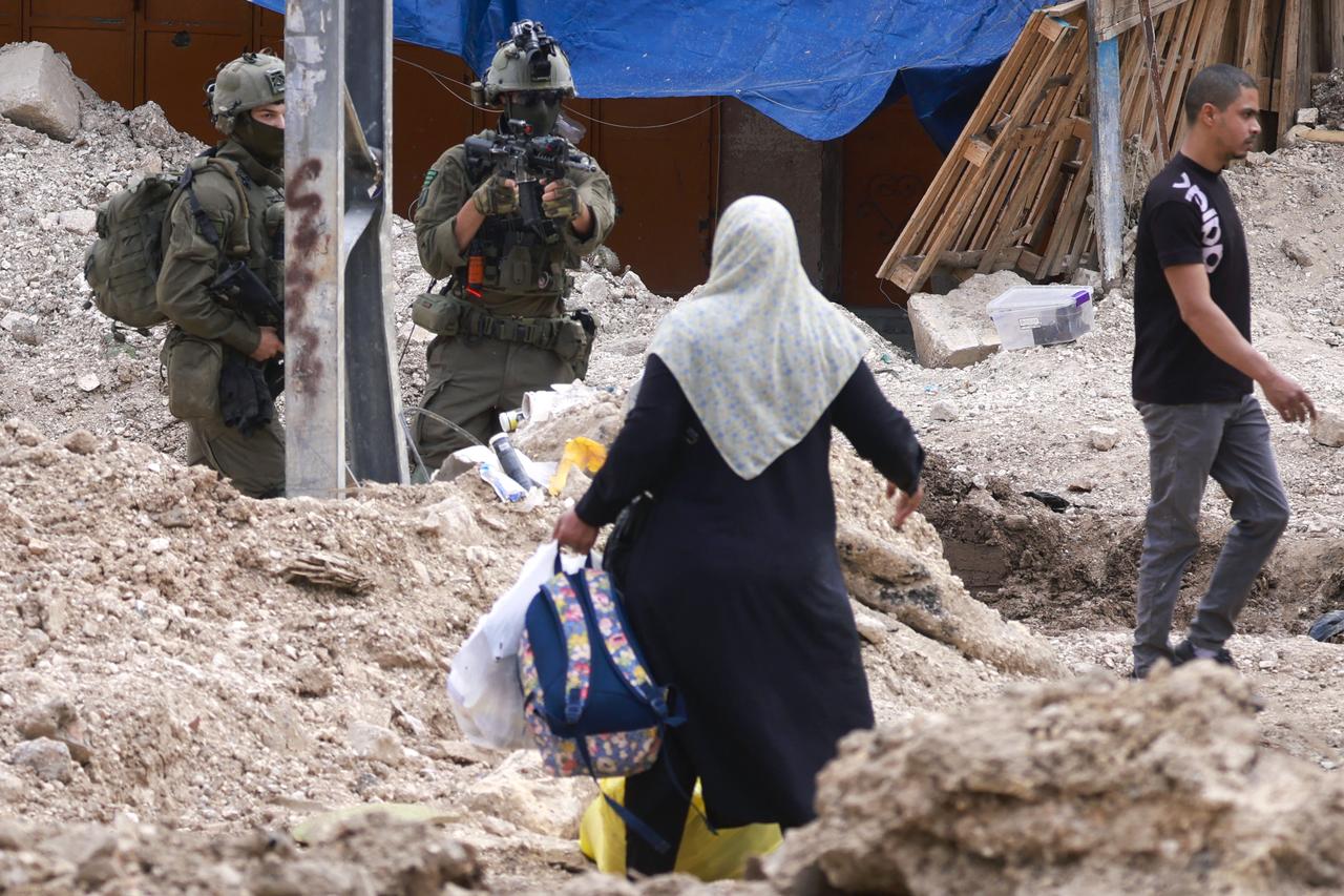 Israeli soldiers look on as Palestinians carry their belongings after being ordered to leave their homes during an Israeli operation in the Tulkarem camp for refugees in the northwest of the occupied West Bank on May 2, 2025. (Photo by Jaafar ASHTIYEH / AFP)