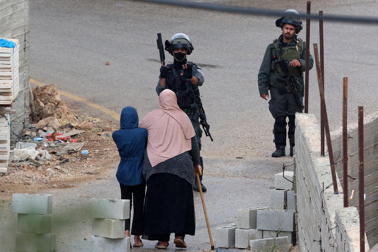 Israeli soldiers look on as Palestinians carry their belongings after being ordered to leave their homes during an Israeli operation in the Tulkarem camp for refugees in the northwest of the occupied West Bank on May 2, 2025. (Photo by Jaafar ASHTIYEH / AFP)
