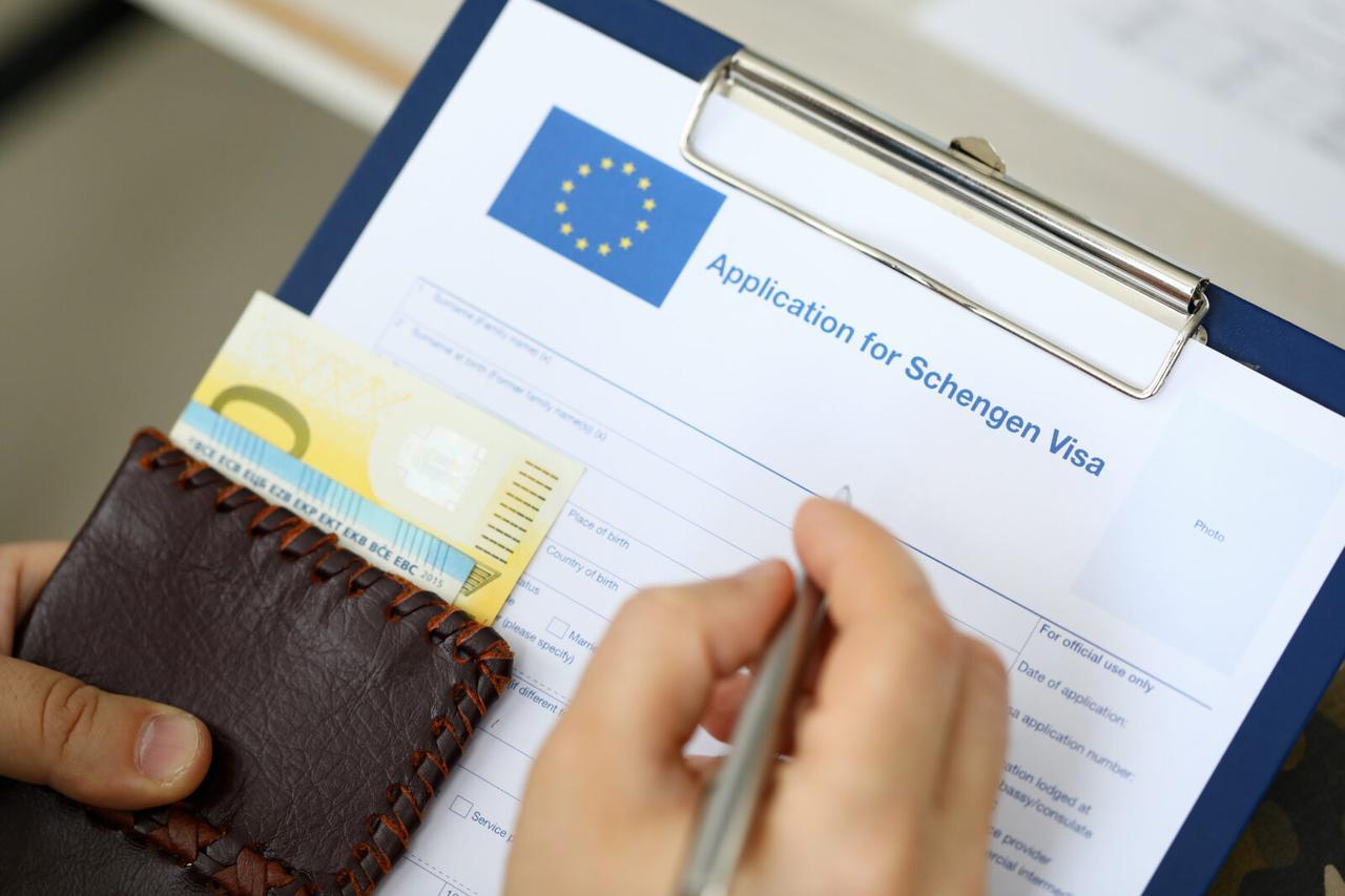 Top view of man filling out documents for Schengen visa while holding money. Travel concept