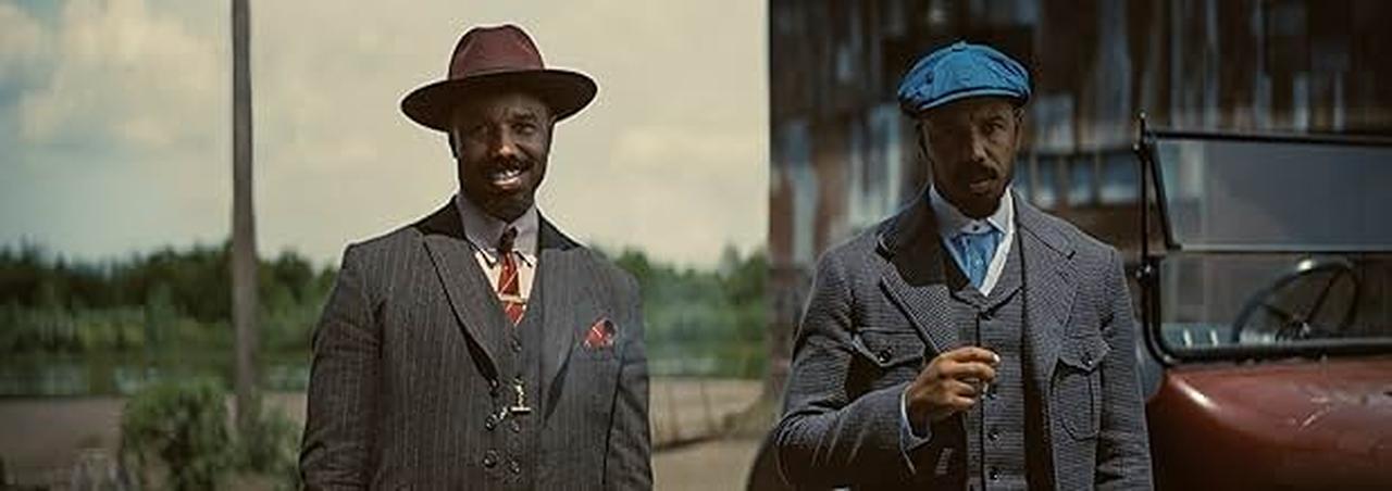 Two sharply dressed characters stand beside a vintage car in a stylized period scene from the film Sinners, accessed on June 1, 2025. (Photo via imdb.com)