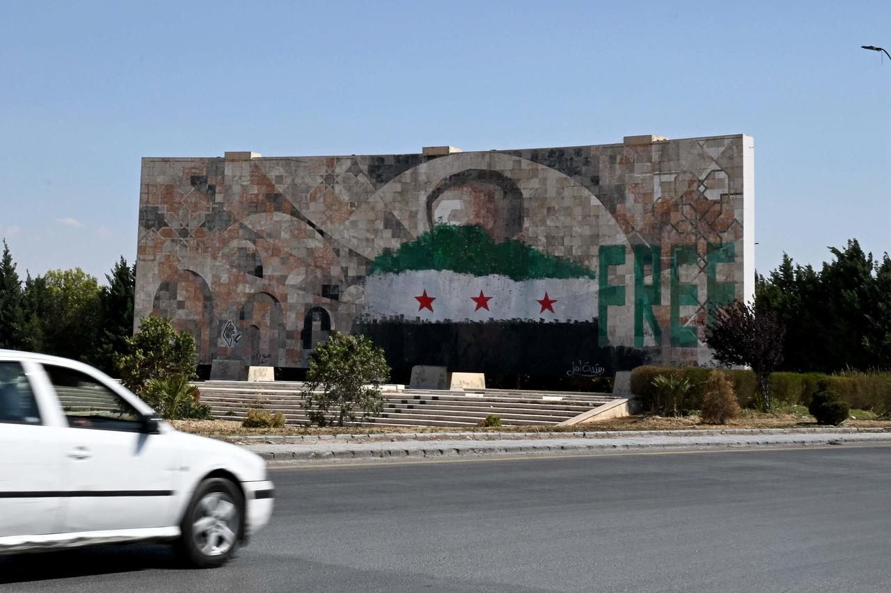 A defaced portrait of former Syrian president Hafez al-Assad with the word "free" and the new Syrian flag stand at the entrance of Damascus on June 3, 2025. (AFP Photo)