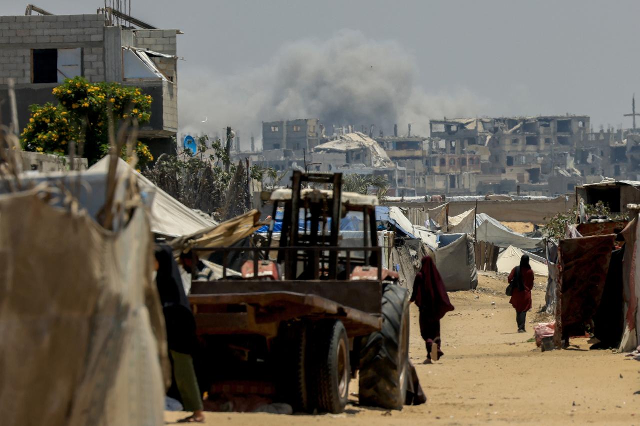 People walk amid shelters in Rafah, in the southern Gaza Strip, as smoke billows during Israeli bombardment on June 11, 2025. (AFP Photo)
