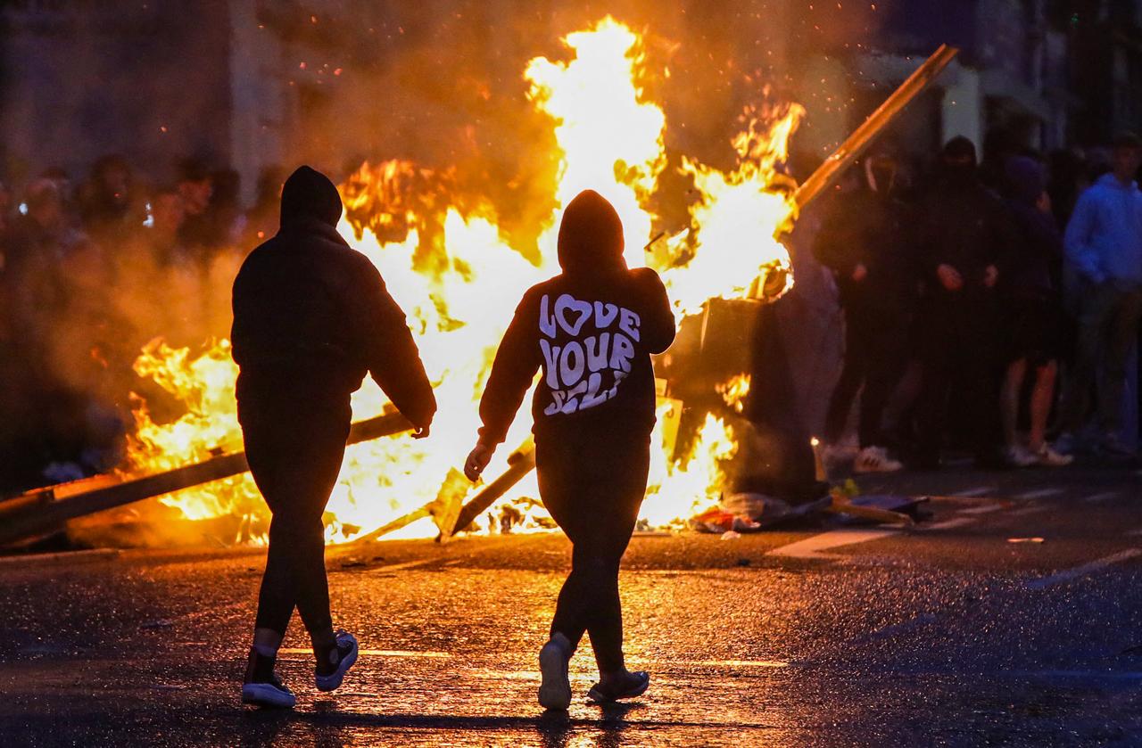 Protestors walk past a fire set in a street of Ballymena, Northern Ireland, during an anti-immigration demonstration, on June 10, 2025. Violence flared for a second night June 10 in the Northern Irish town of Ballymena after  racially motivated  attacks sparked by the arrest of two teenagers accused of the attempted rape of a young girl. Hundreds of protestors, many of them masked, took to the streets of Ballymena, throwing petrol bombs and masonry as police responded with water cannon, an AFP journalist said. (Photo by PAUL FAITH / AFP)