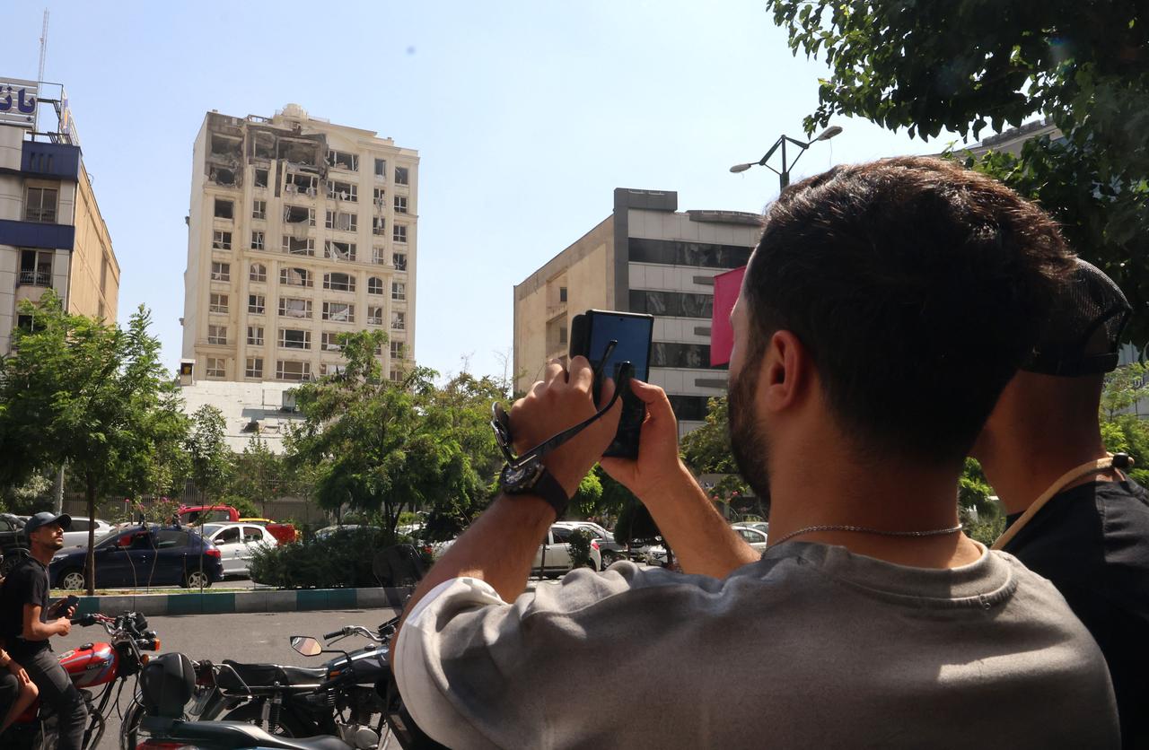 A man takes a picture of a building damaged in an Israeli strike on Tehran on June 13, 2025. Israel hit about 100 targets in Iran on June 13, including nuclear facilities and military command centres and killing senior figures. (AFP Photo)