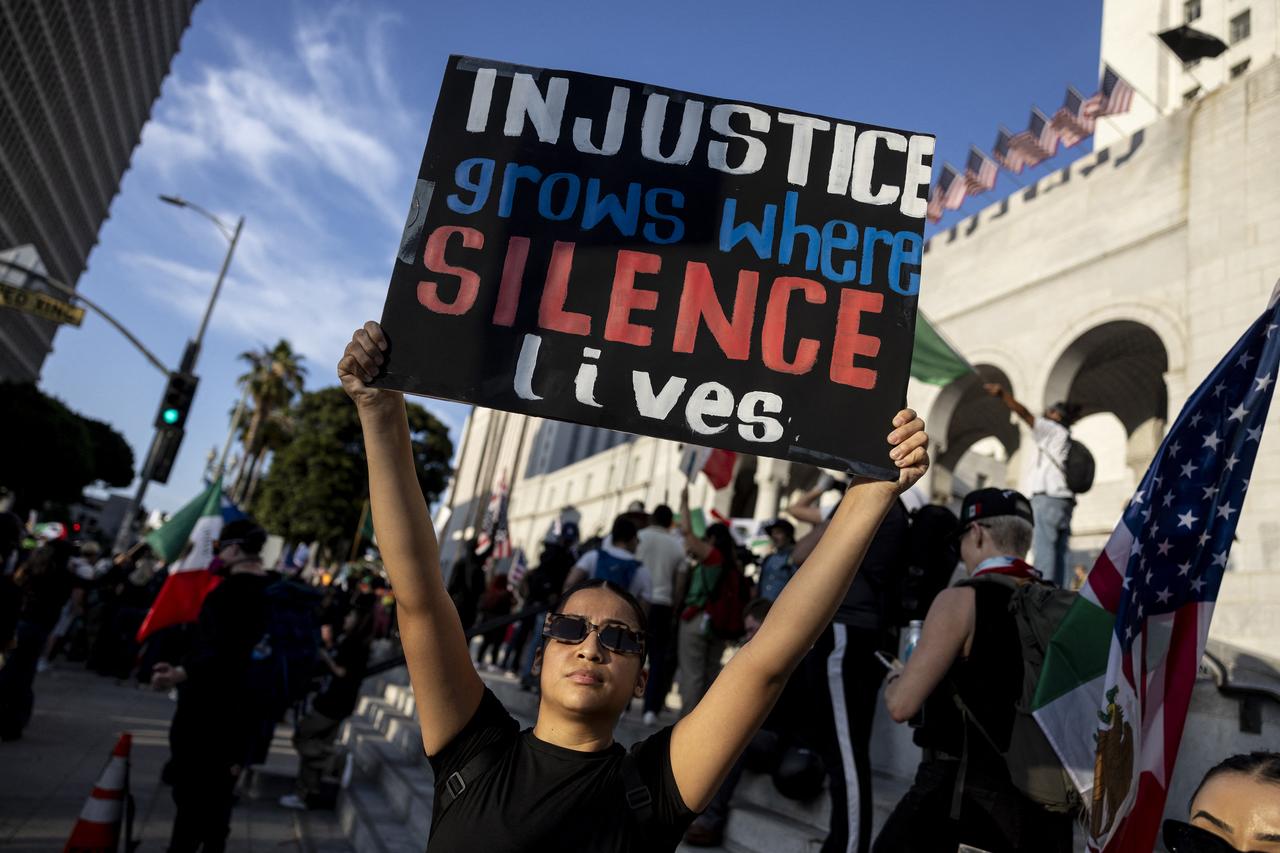 A demonstrator holds a sign reading "Injustice grows where silence lives" in front of City Hall as protests continue in response to federal immigration operations in Los Angeles on June 13, 2025. (AFP Photo)