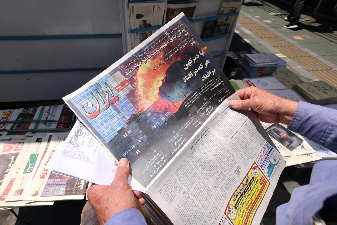 A man looks at an Iranian daily newspaper, displaying an image of an explosion in Israel, at a newstand in Tehran on June 15, 2025. Israel pressed its intense bombardment campaign on Iran on June 15, striking a defence facility and fuel depots as the two arch foes kept up their most intense confrontation in history. (Photo by ATTA KENARE / AFP)