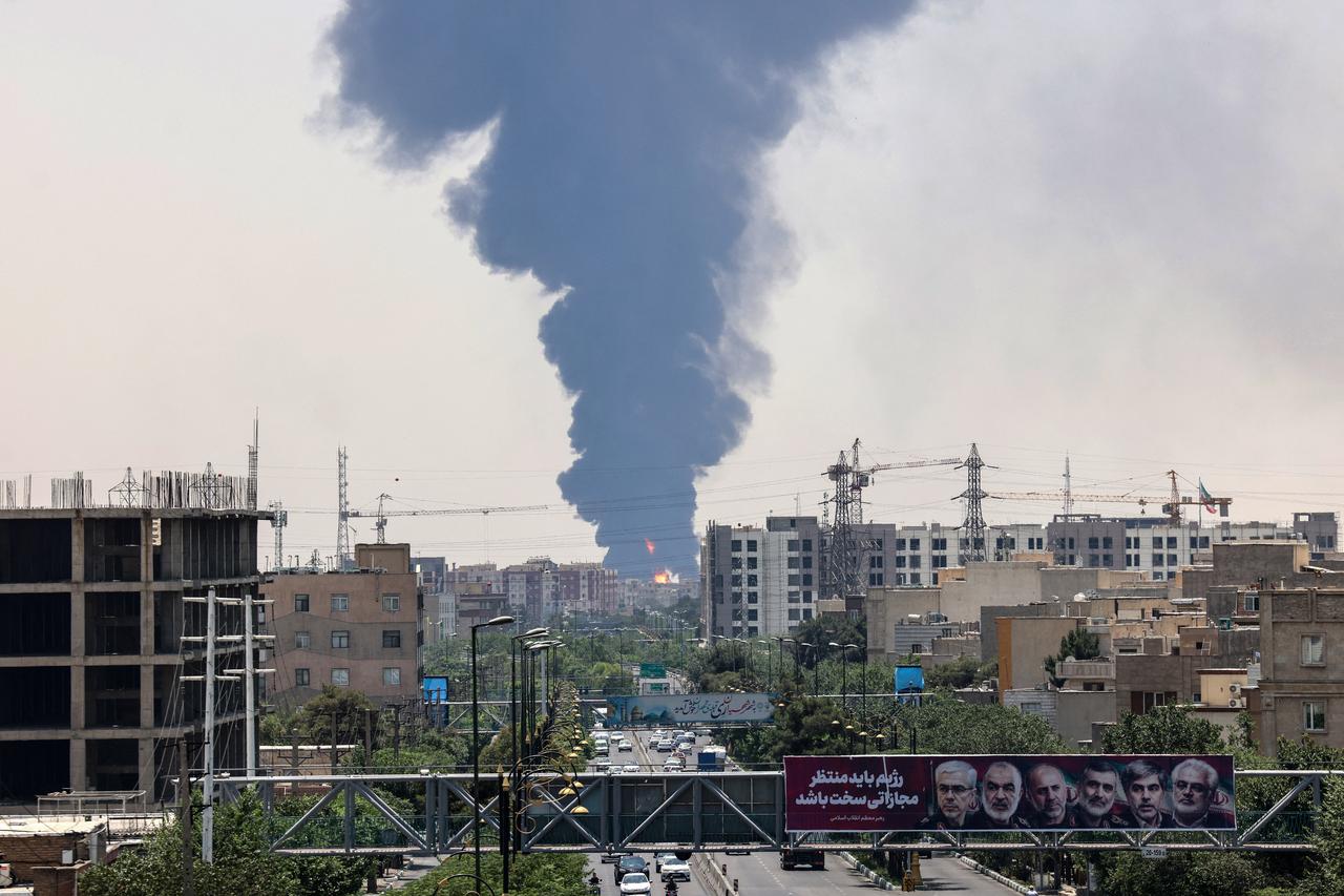 Portraits of Iranian military generals and nuclear scientists, killed in Israels June 13 attack are displayed above a road, as a plume of heavy smoke and fire rise over an oil refinery in southern Tehran, after it was hit in an overnight Israeli strike, on June 15, 2025. Iran fired a fresh barrage of missiles at Israel, state television announced early on June 15, as the rivals exchanged fire for a third day. (Photo by ATTA KENARE / AFP)