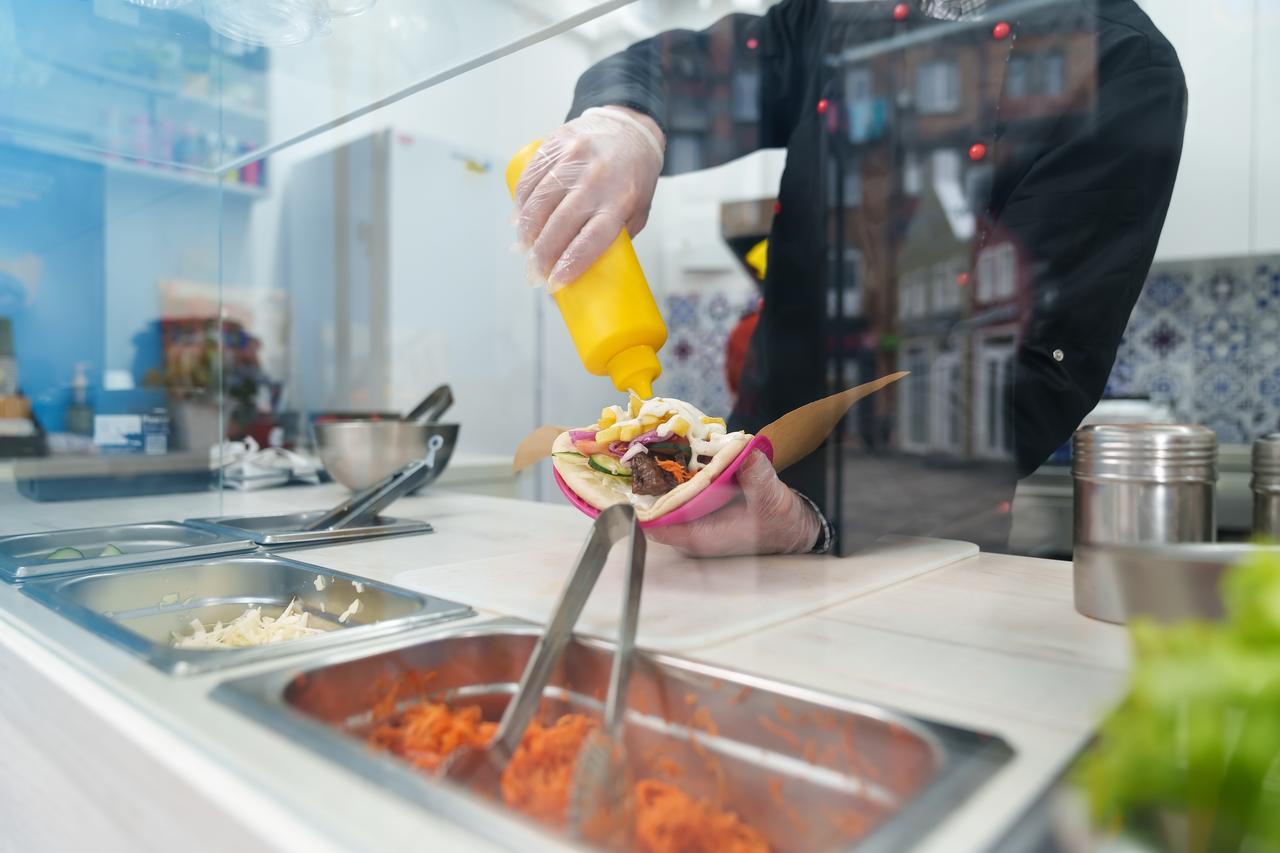 Cook pouring tzatziki sauce on souvlaki meat in Greek fast food restaurant kitchen. (Adobe Stock Photo)