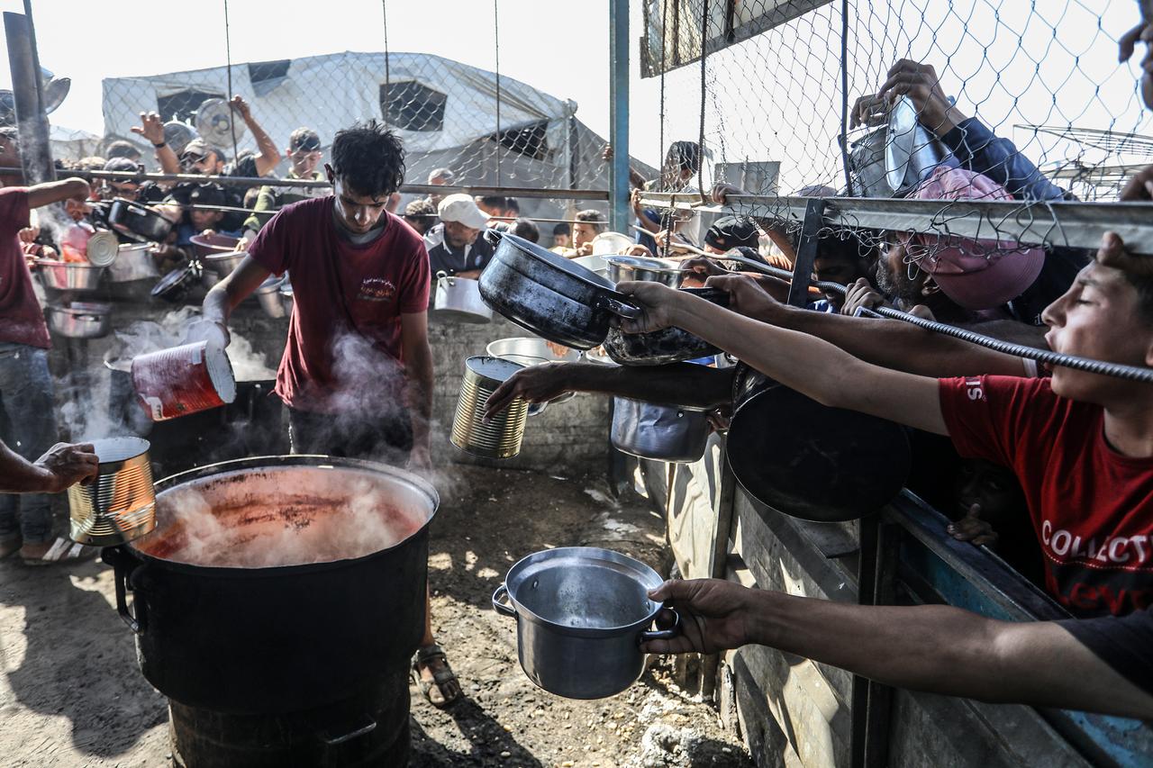 Displaced Palestinians receive hot meals distributed by aid organizations in al-Mawasi area of Khan Yunis, Gaza on June 20, 2025. (AA Photo)