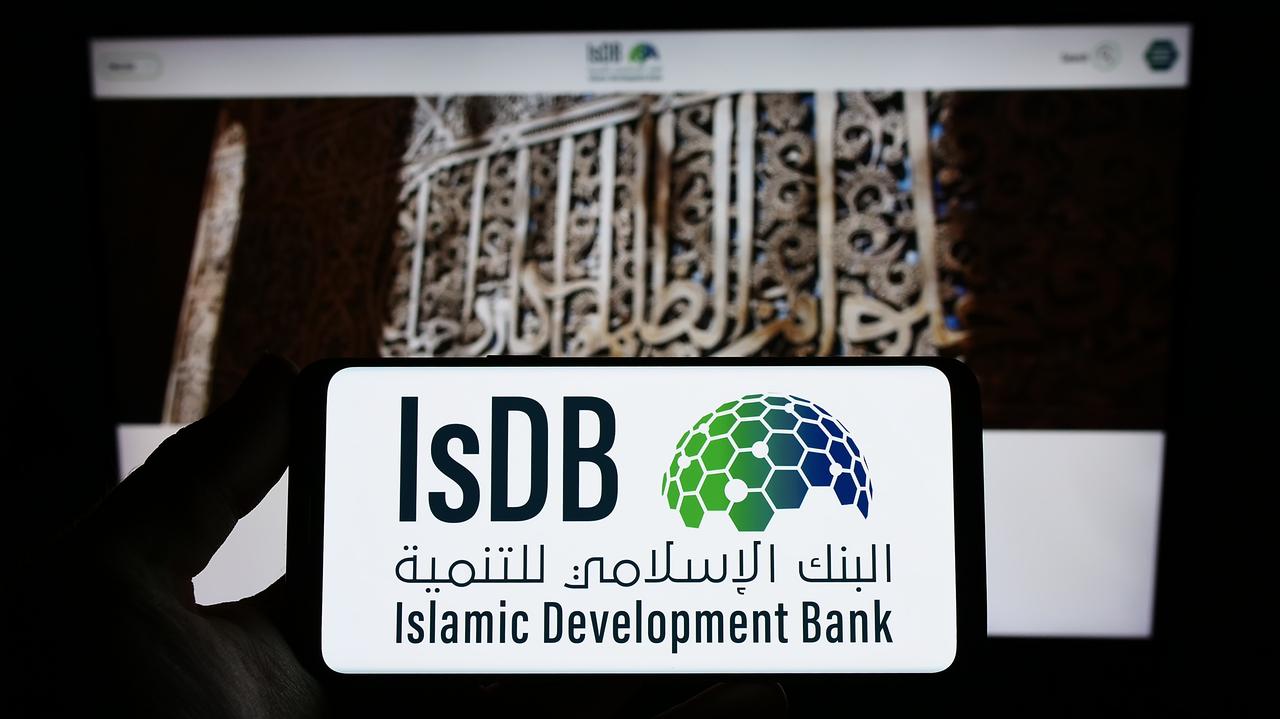 Photo illustration shows a person holding a smartphone displaying the Islamic Development Bank (IsDB) logo in front of the bank’s official website in Stuttgary, Germany, on March 19, 2023. (Adobe Stock Photo)