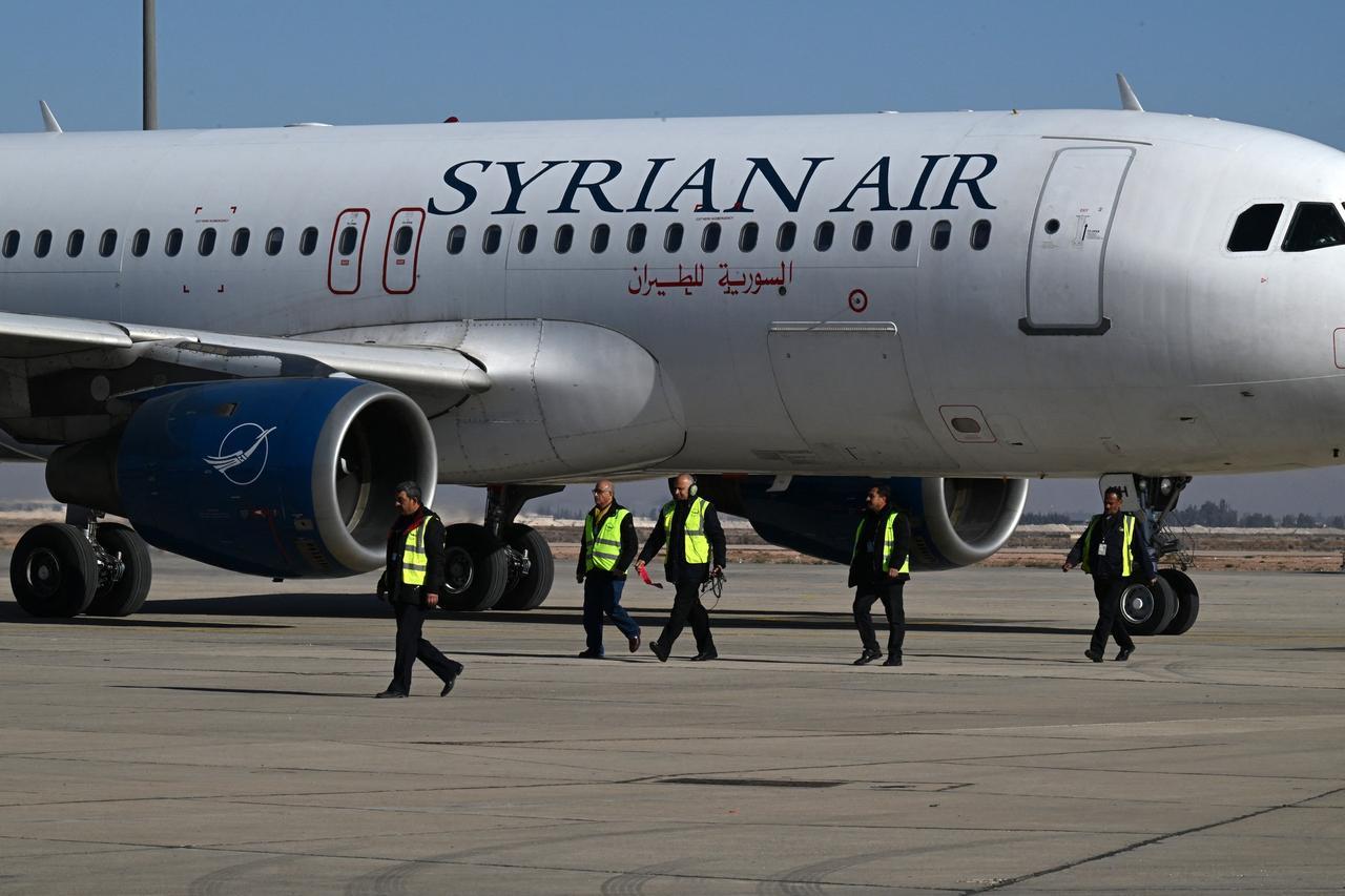 Ground personnel walk on the tarmac as a Syrian Air aircraft taxis ahead of take off to the city of Aleppo, on Dec. 18, 2024. (AFP Photo) 