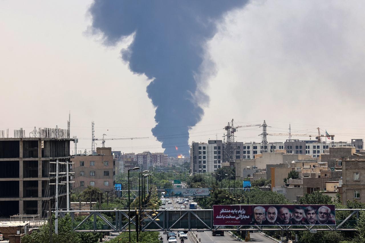 Portraits of Iranian military generals and nuclear scientists, killed in Israels June 13 attack are displayed above a road, as a plume of heavy smoke and fire rise over an oil refinery in southern Tehran, after it was hit in an overnight Israeli strike, on June 15, 2025. (AFP Photo)