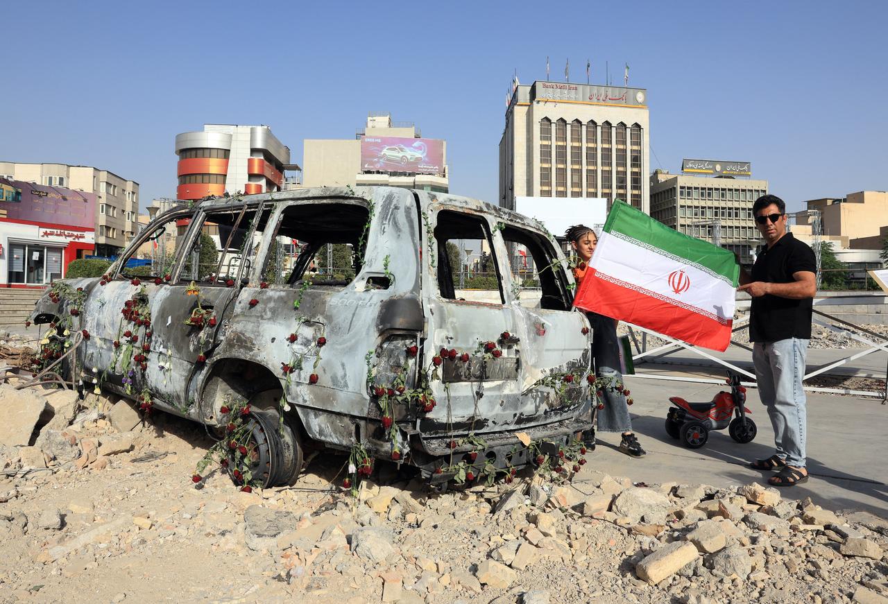 A man holds an Iranian flag by an Iranian Red Crescent ambulance that was destroyed during an Israeli strike, displayed in Tehran on June 23, 2025. (AFP Photo)