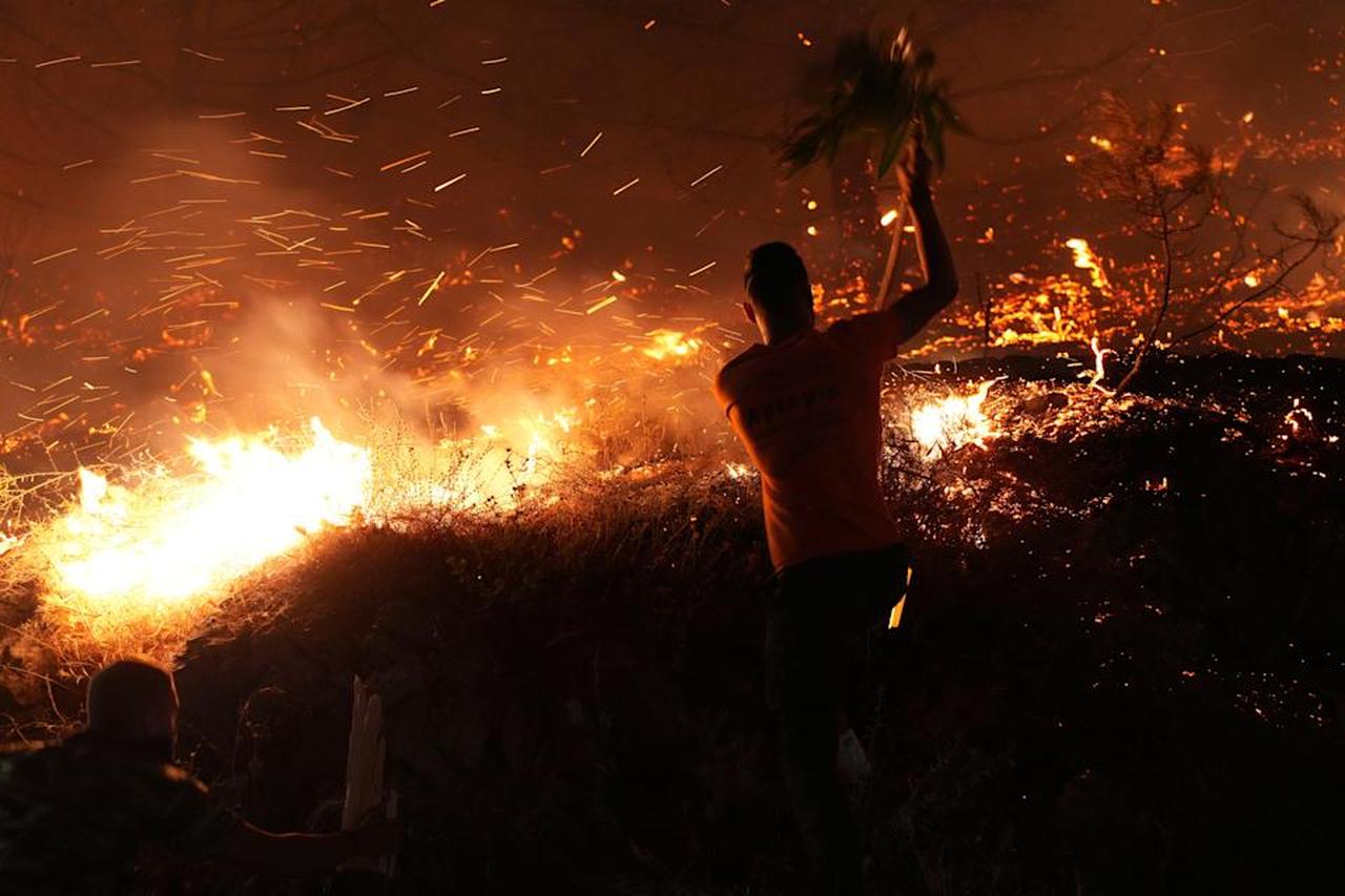 A man uses a branch to battle against a large wildfire burning in Kofinas, on the eastern Aegean island of Chios, Greece, late Sunday, June 22, 2025. (Photo via Politischios.gr)
