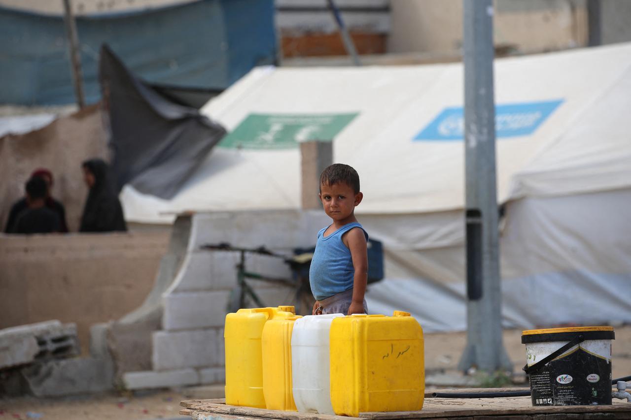 A Palestinian boy waits next to water containers as people queue at a water distribution point in Nuseirat, in the central Gaza Strip, on June 23, 2025. (AFP Photo)