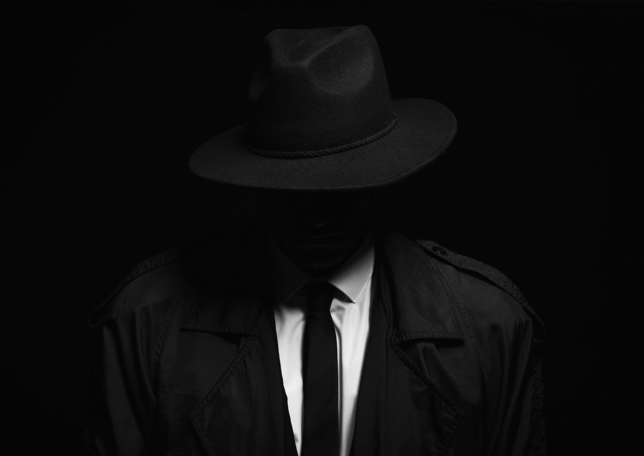Old fashioned detective in hat on dark background. (Adobe Stock Photo)