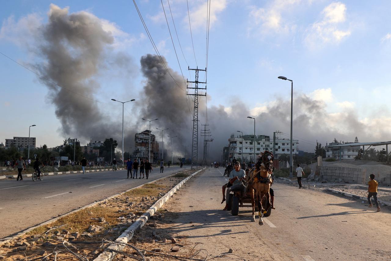 Smoke plumes rise during an Israeli strike as Palestinians riding a horse-pulled cart speed along the Salah al-Din road near the Nusseirat refugee camp in the central Gaza Strip on June 25, 2025. (AFP Photo)