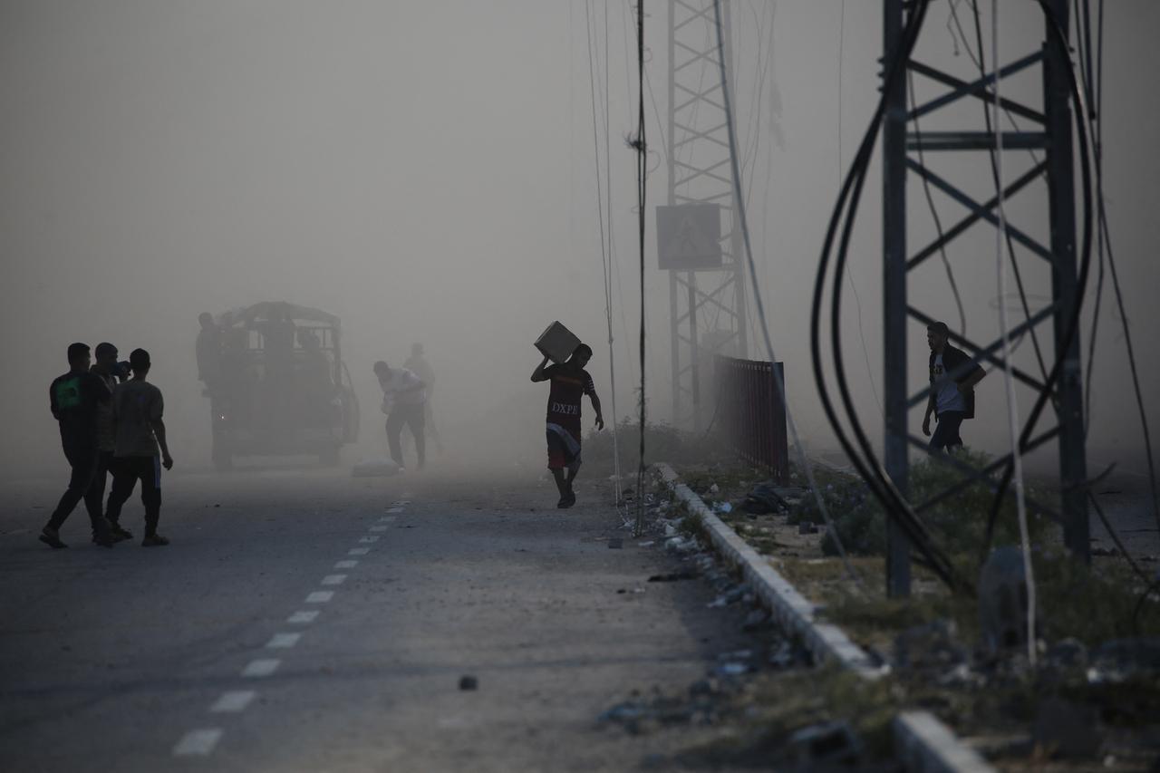 A Palestinian man carries a parcel as he walks with others amid the smoke from an Israeli strike, along the Salah al-Din road near the Nusseirat refugee camp in the central Gaza Strip on June 25, 2025. (AFP Photo)