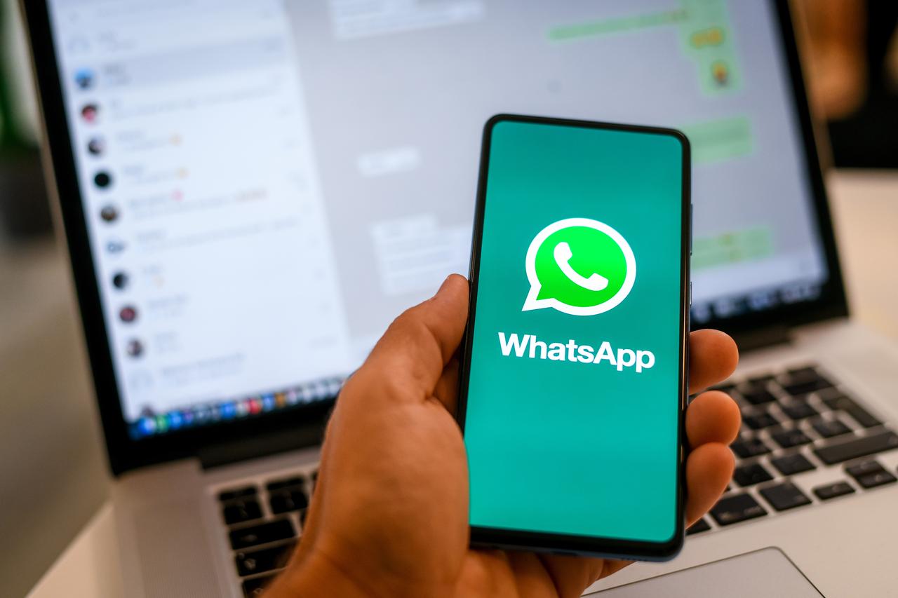 Close-up of a hand holding a smartphone with the WhatsApp logo displayed, with a laptop in the background in Milan, Italy, on October 2021. (Adobe Stock Photo)