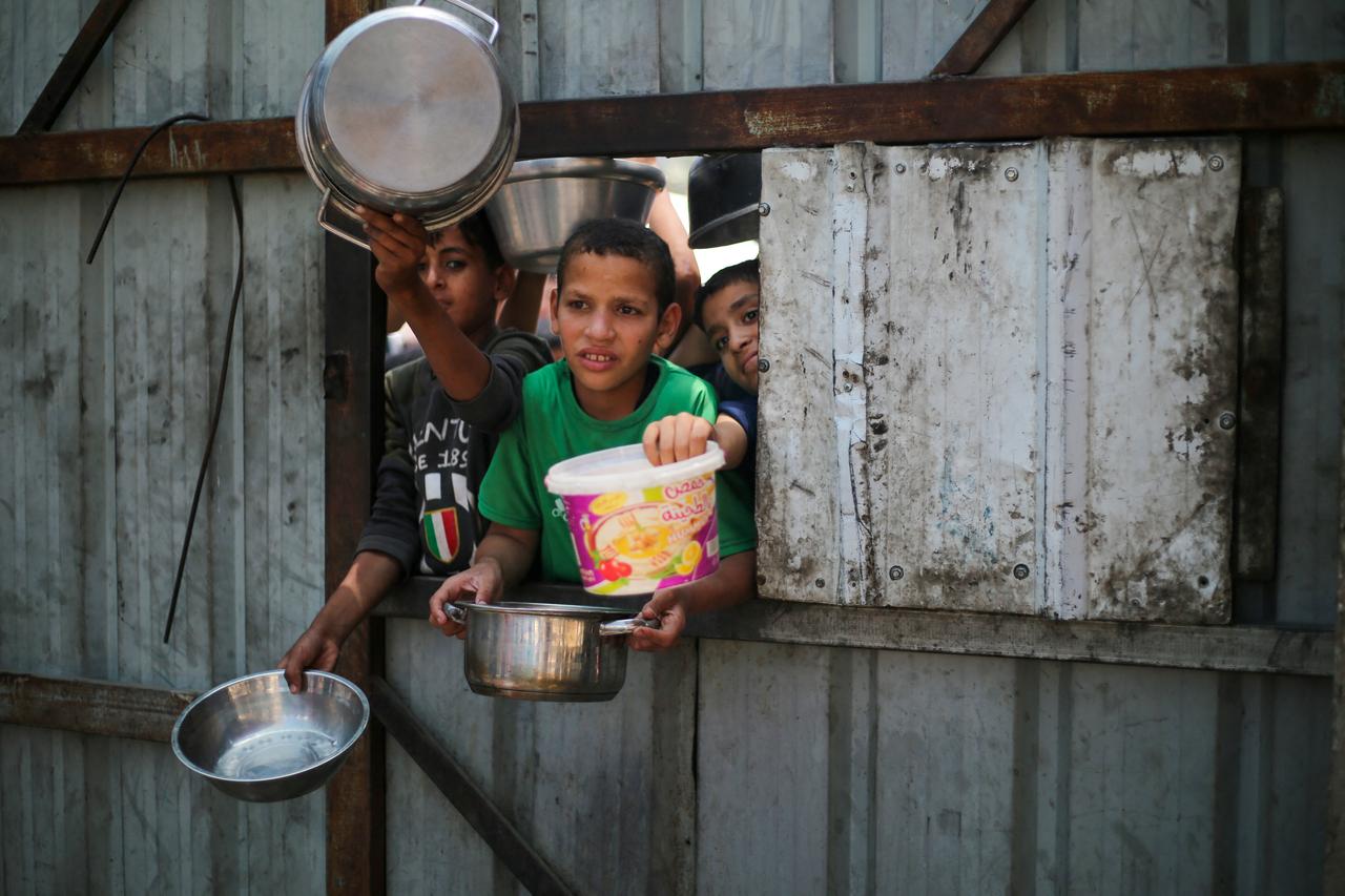 Palestinian children reach out with their pots as they wait for food at a distribution point in Nuseirat, central Gaza Strip, June 2, 2025. Israel has faced growing condemnation over the humanitarian crisis in the war-ravaged Gaza Strip, where the United Nations has warned the entire population faces the risk of famine after no aid was allowed to enter for more than two months. (Photo by Eyad BABA / AFP)