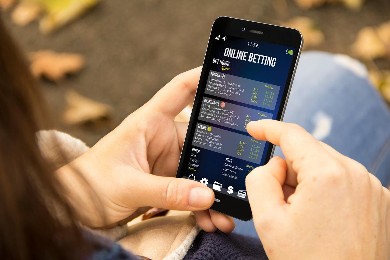 A young woman betting online at the park. (Adobe Stock Photo)