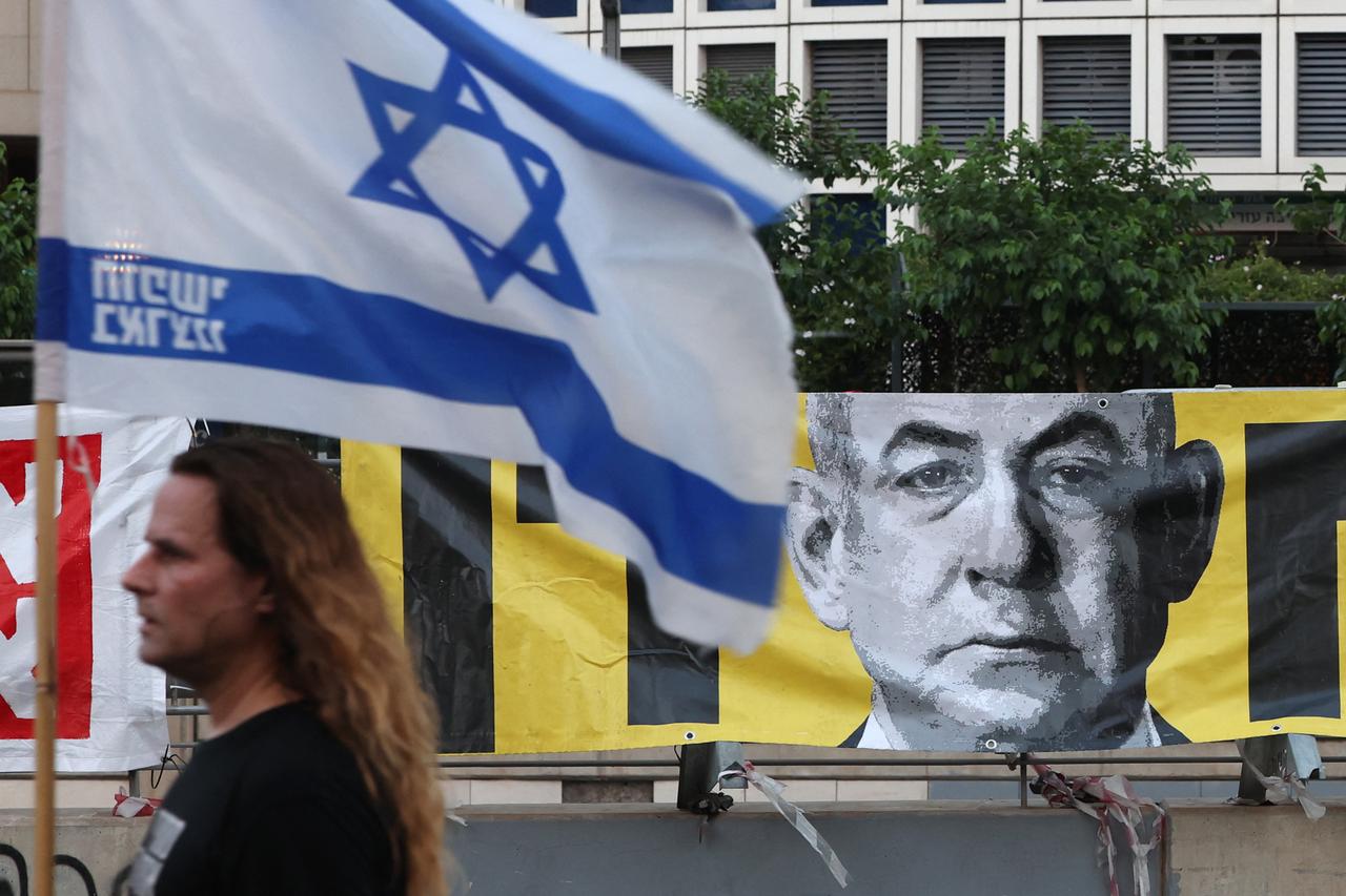 A demonstrator carrying the Israeli flag walks past a portrait of Prime Minister Benjamin Netanyahu, in front of the Defence Ministry in Tel Aviv on June 7, 2025,. (AFP Photo)