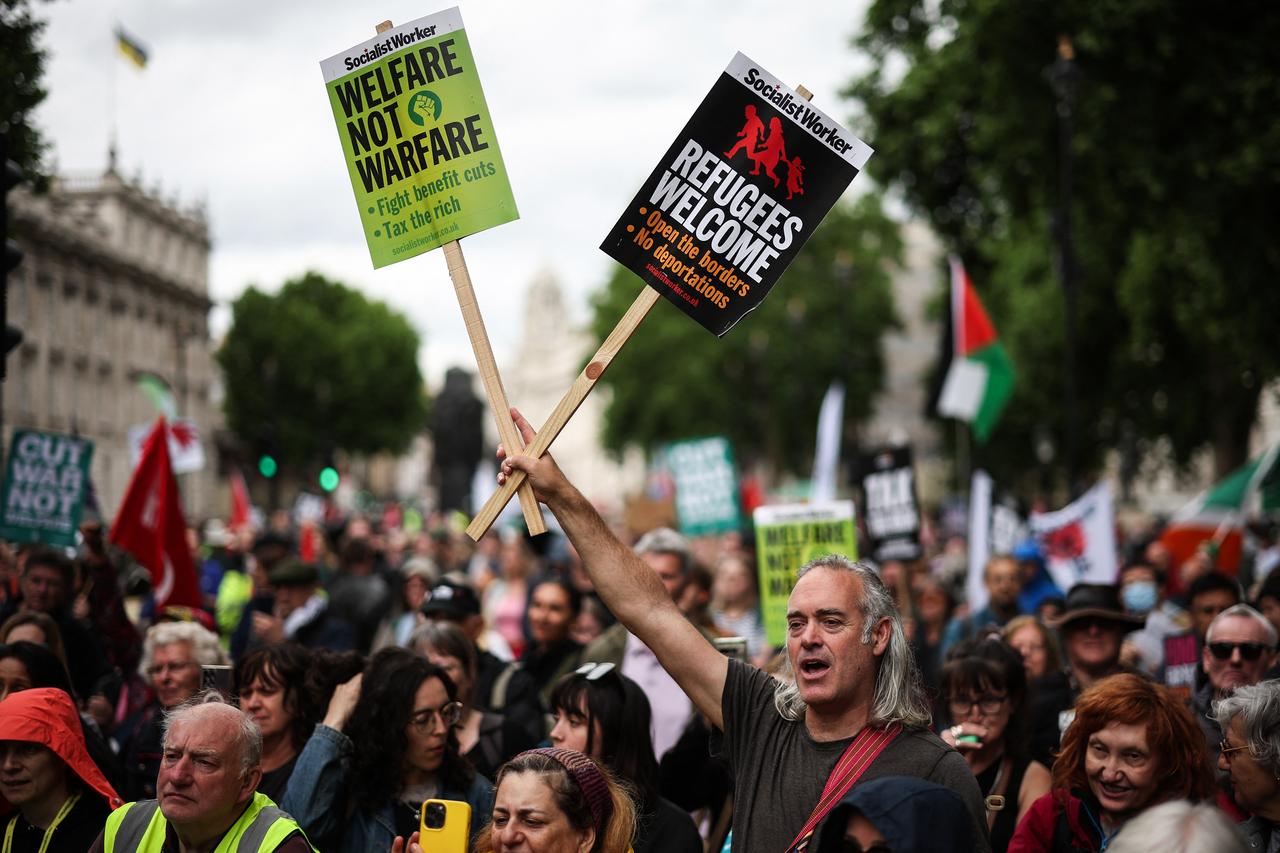 A protester holds placards reading "Welfare not warfare" and "Refugees welcome" during a "No More Austerity 2.0" march in central London on June 7, 2025. (AFP Photo)