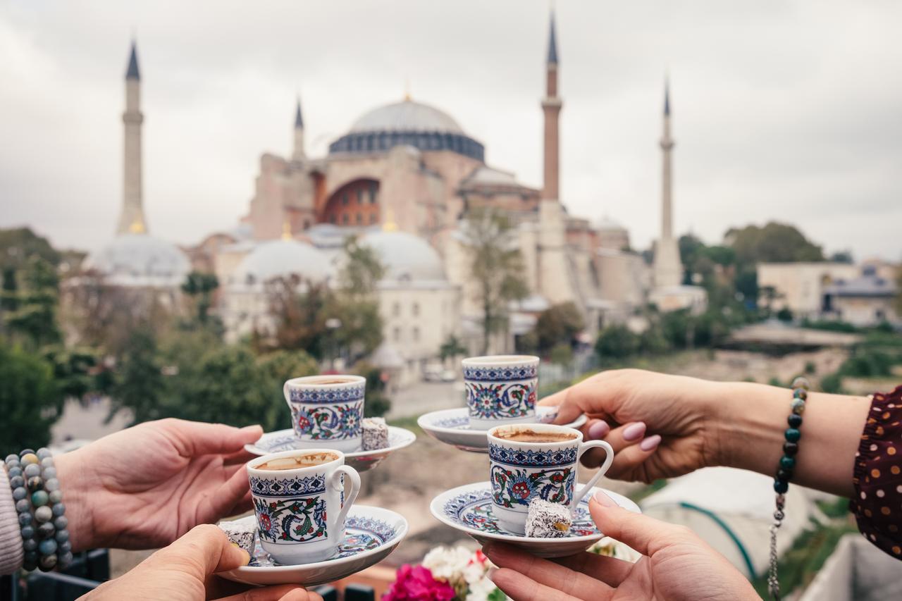 Hands hold traditional Turkish coffee cups in front of Hagia Sophia, in Istanbul, Türkiye. (Adobe Stock Photo)