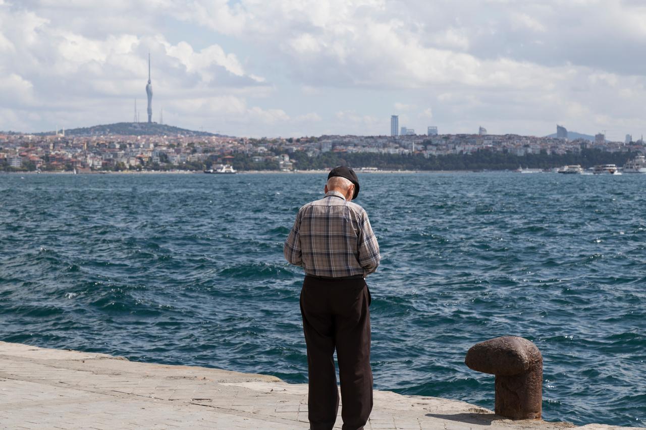 An elderly man stands alone by the waterfront facing the Bosphorus, in Istanbul, Türkiye. (Adobe Stock Photo)