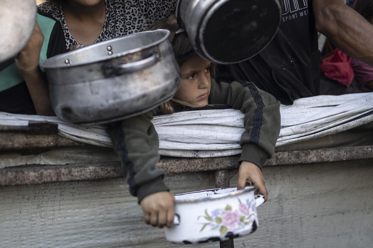A Palestinian child holds an empty pot while waiting to receive food distributed by a charity in the Al-Rimal neighborhood of Gaza City, July 11, 2025. (AA Photo)