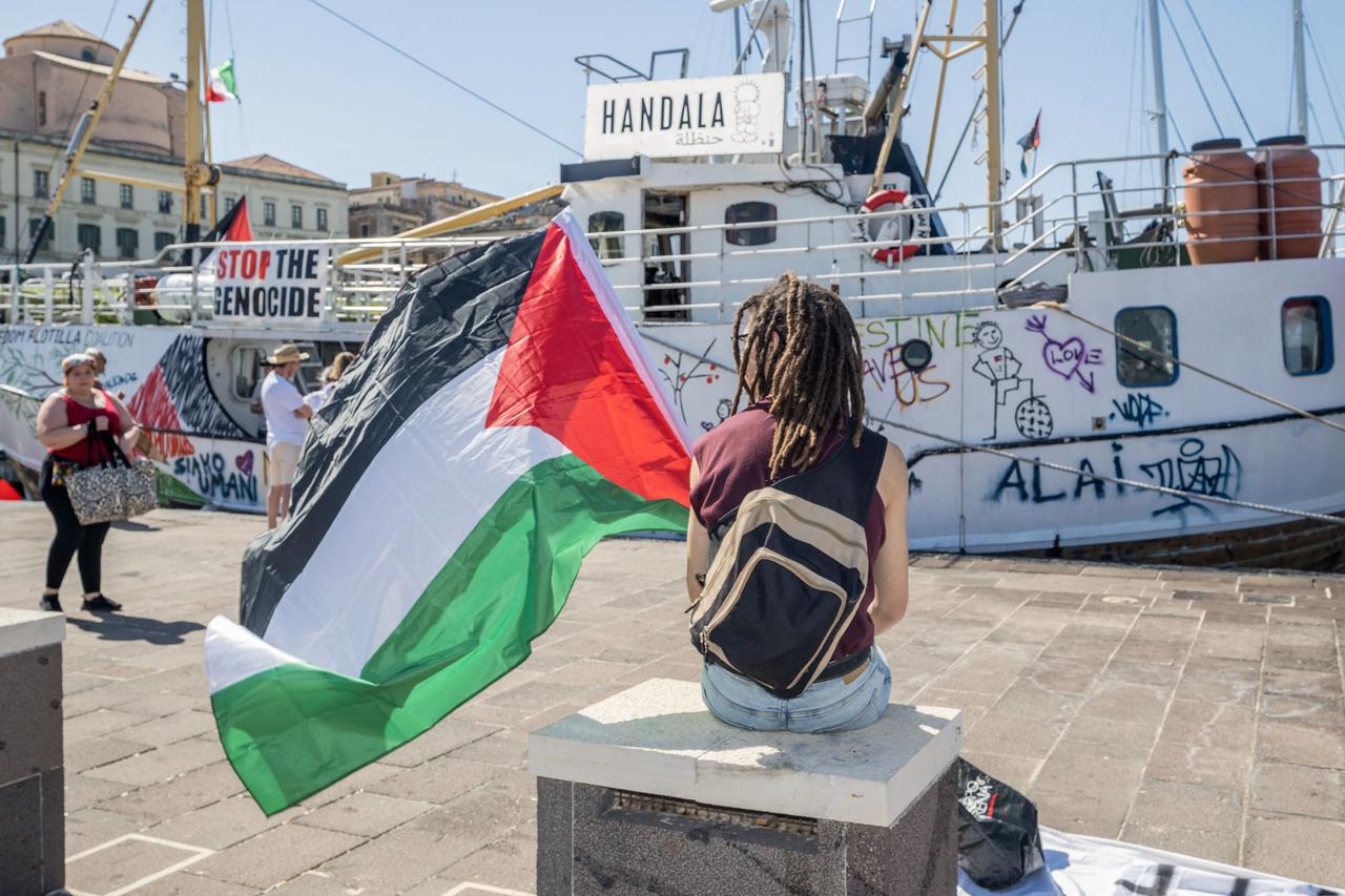 A person holds a Palestinian flag in front of the docked Freedom Flotilla ship "Handala" ahead of the boat's departure for Gaza at a port in Syracuse, Sicily, southern Italy, July 13, 2025. (Photo by AFP)