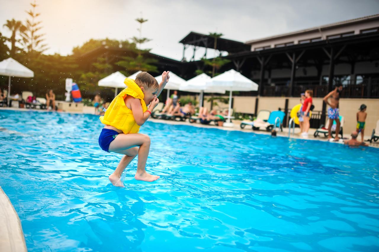 A young boy wearing a life vest jumps into a hotel swimming pool in Türkiye. (Adobe Stock Photo)