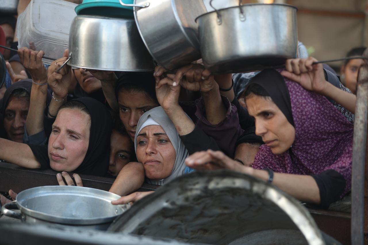 Palestinians, including children struggle to receive hot meals distributed by a local charity in Gaza City on July 14, 2025. (AA Photo)