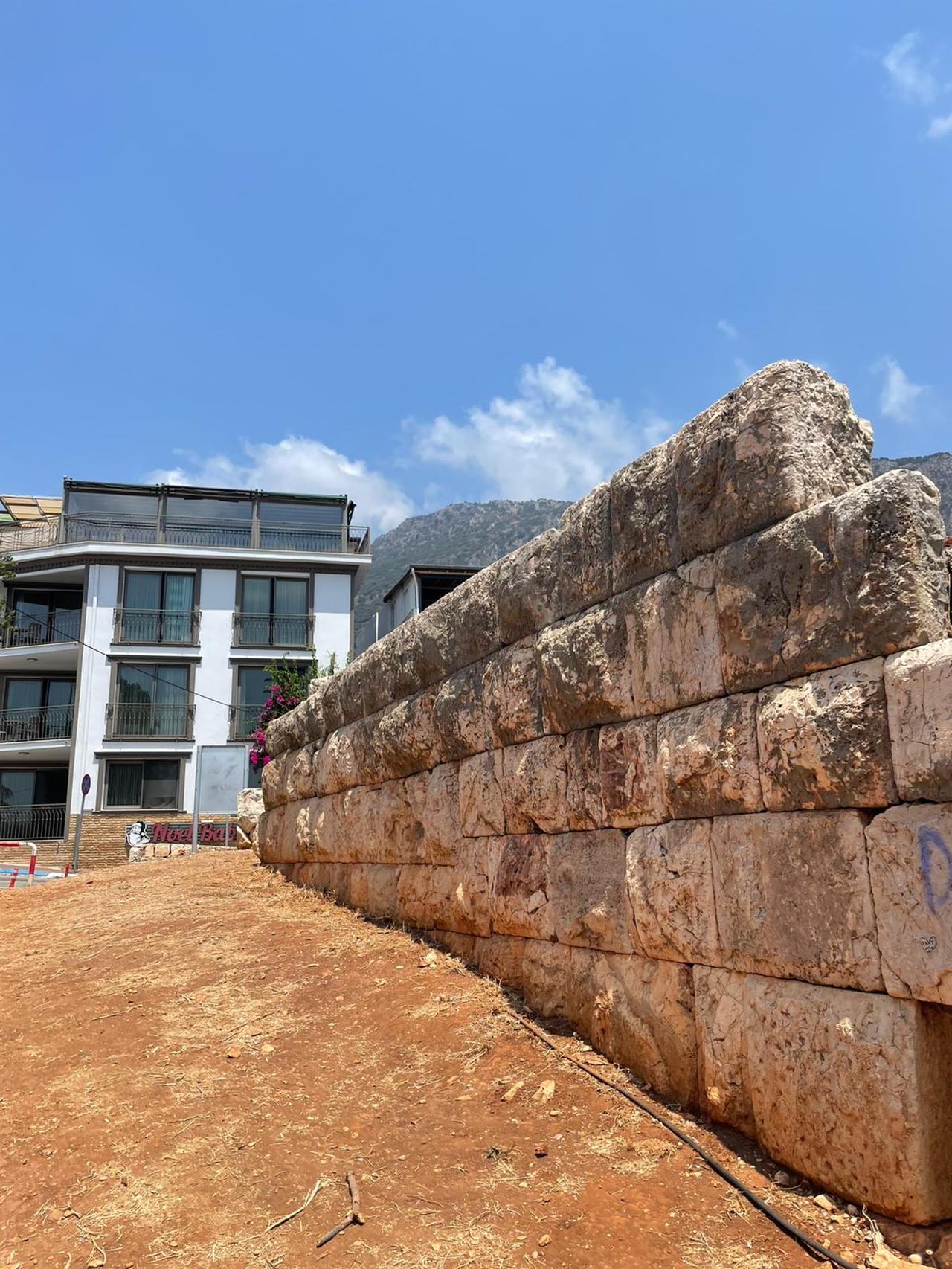 Stone ruins of a Hellenistic-period temple stand amidst modern buildings and lush vegetation in the town center of Kas, Antalya, Türkiye, July 17, 2025. (Photo via Koray Erdogan/Türkiye Today)