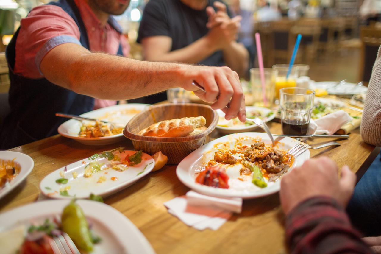 People enjoy a shared dinner with meat dishes, salads, and drinks at a casual restaurant in Istanbul, Türkiye, accessed July 18, 2025. (Adobe Stock Photo)
