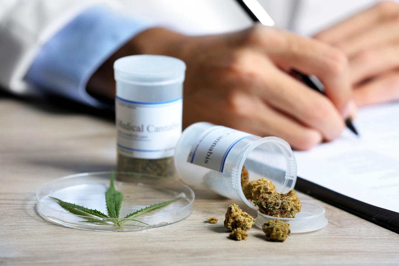 Doctor writes on prescription pad next to bottle of medical cannabis on table. (Adobe Stock Photo)