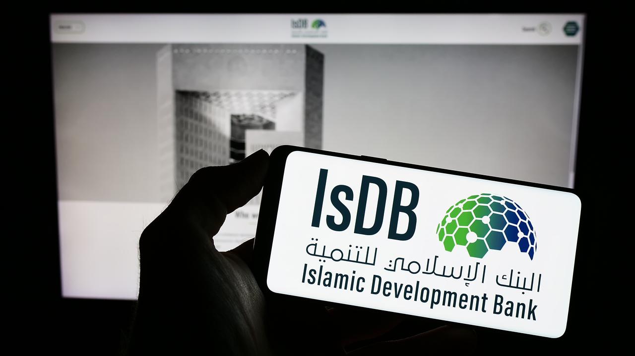 The image shows a hand holding a smartphone displaying the logo of the Islamic Development Bank (IsDB). (Adobe Stock Photo)