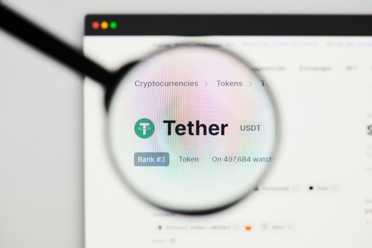 Photo illustration shows a magnifying glass hovering over the Tether logo on its website. (Adobe Stock Photo)