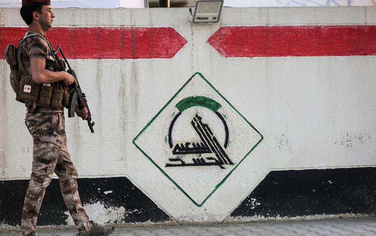 A fighter of Iraq's Popular Mobilization Forces stands guard next to a wall showing the group's logo outside their headquarters in the capital Baghdad on June 13, 2021. (AFP Photo)