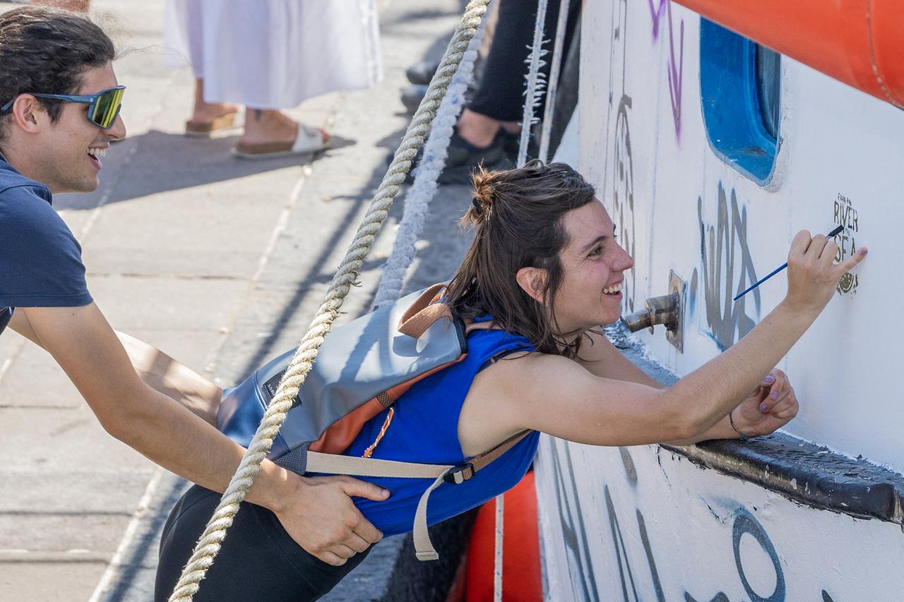 A woman paints the slogan "From the River to the Sea" on the Freedom Flotilla ship "Handala" ahead of the boat's departure for Gaza at a port in Syracuse, Sicily, southern Italy, on July 13, 2025.(Photo by AFP)