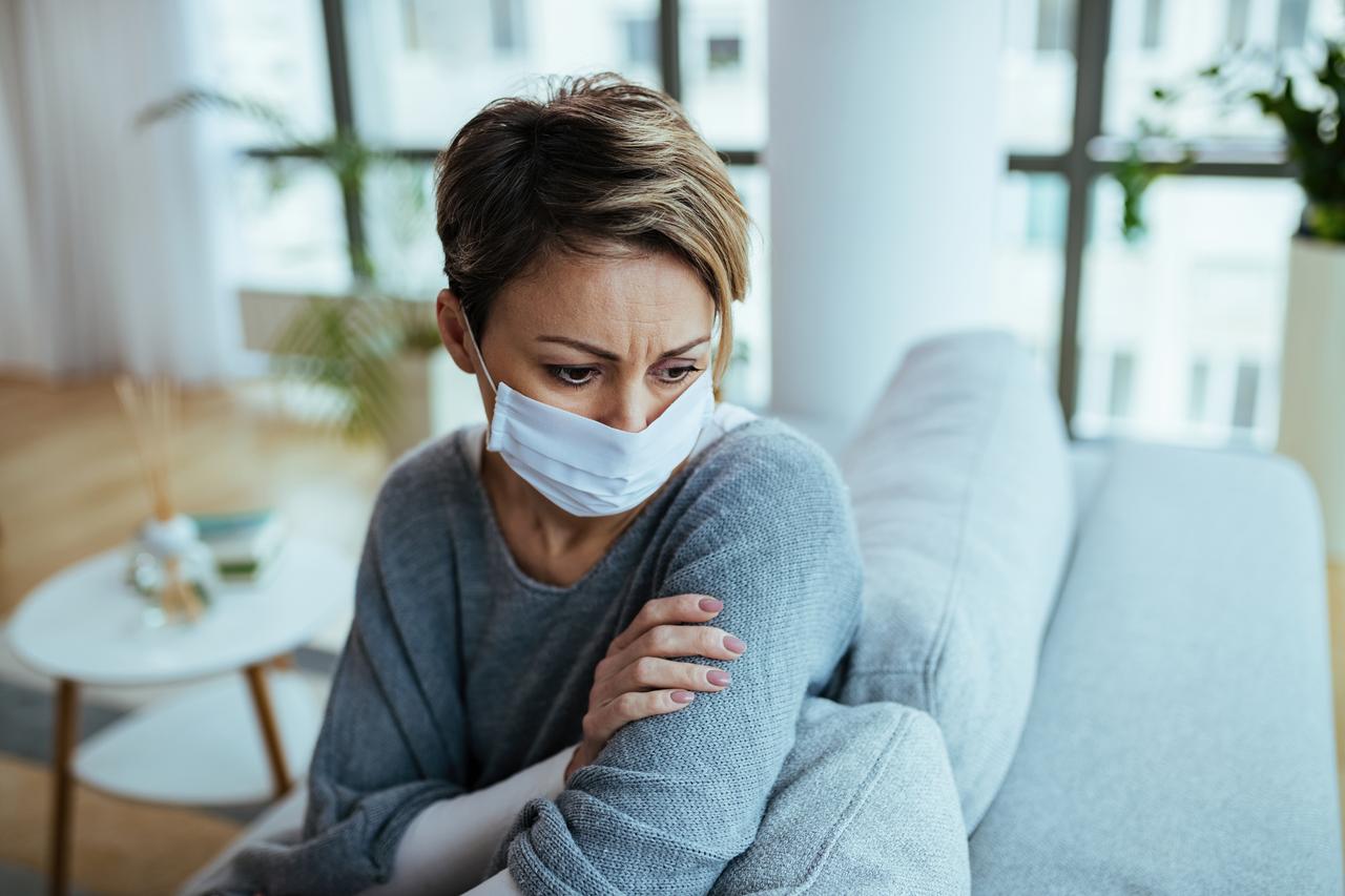 Depressed woman in a face mask deep in thought while staying indoors during the COVID-19 lockdown. (Adobe Stock Photo)