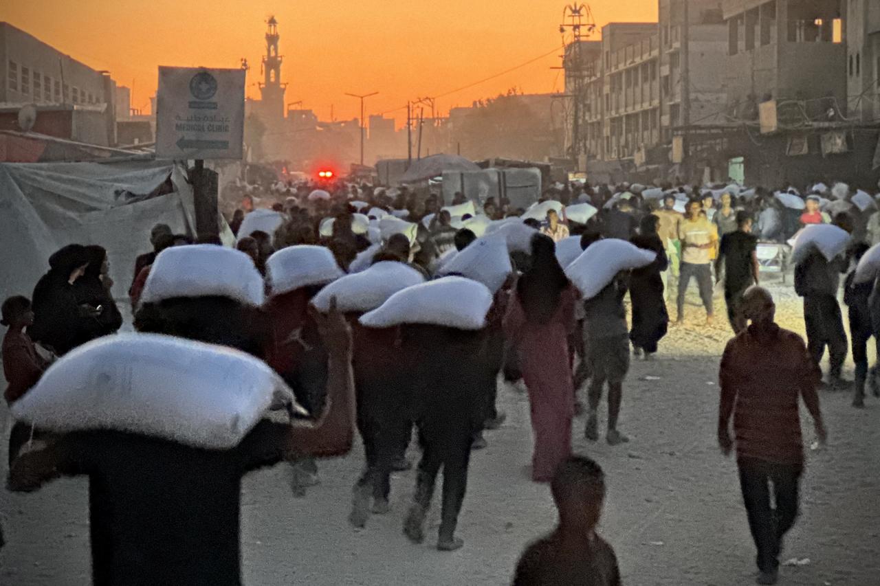 Men walk carrying sacks of flour that were taken from a raided truck carrying foodstuffs, in Khan Yunis in the southern Gaza Strip on July 22, 2025. (AFP Photo)
