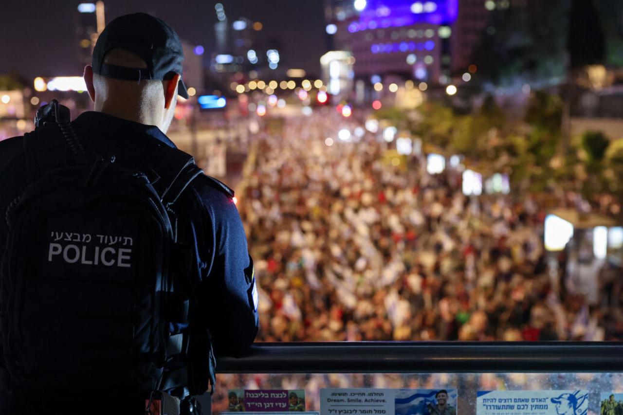 An Israeli police man stands guard as relatives and supporters of hostages hold placards and wave national flags during a demonstration in Tel Aviv on May 4, 2024. (AFP Photo)