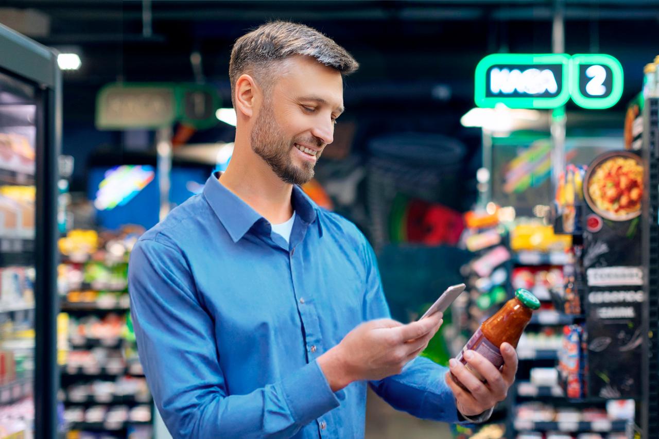 A man is using his smartphone to scan a QR code that is placed on a glass jar, carefully holding his device close to the code to access detailed information about the product. (Adobe Stock Photo)
