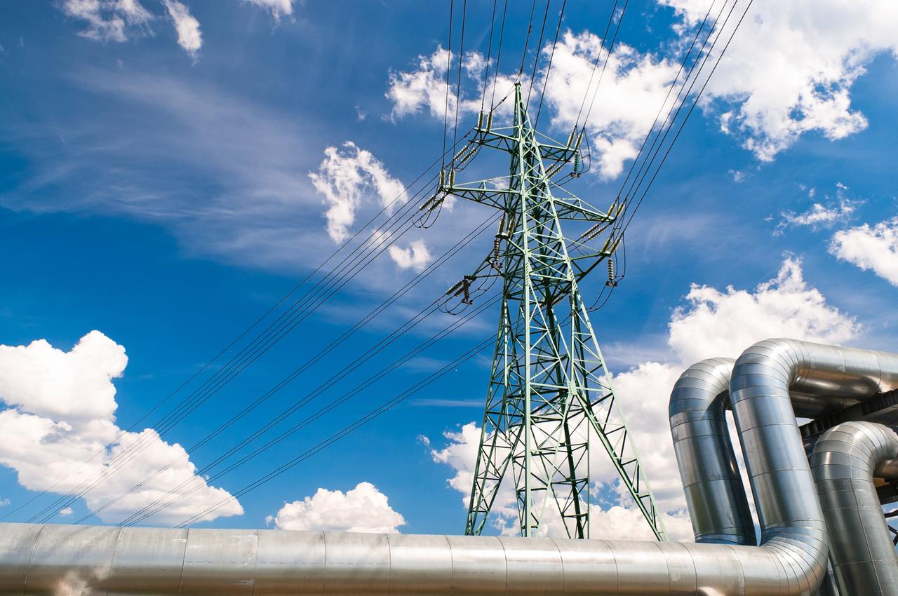 High-voltage power lines and industrial gas pipelines illustrate the intersection of electricity transmission and energy infrastructure. (Adobe Stock Photo)