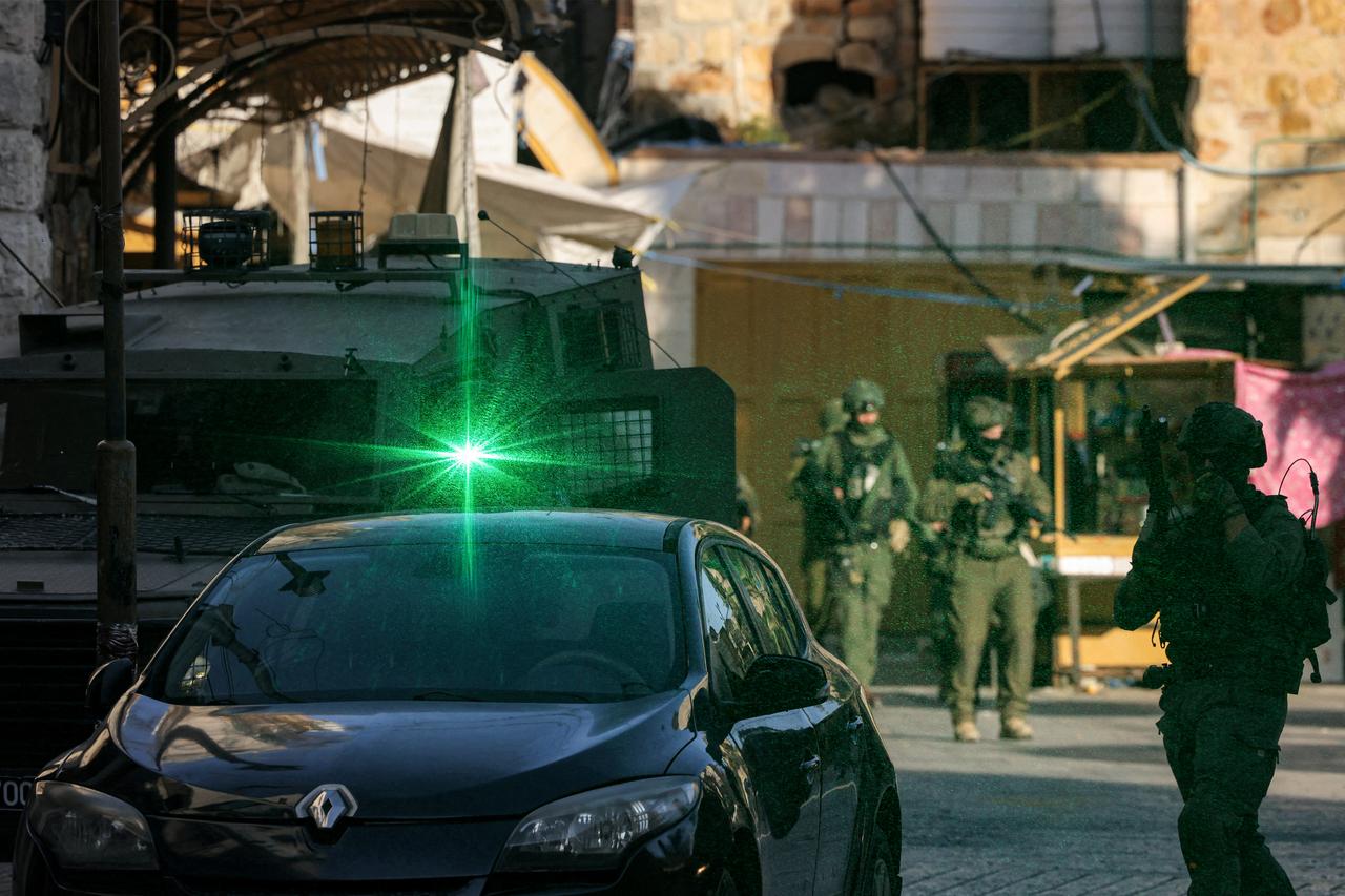An Israeli soldier points his laser target towards the photographer while standing guard as Israeli settlers tour in the old city-centre and market of the Palestinian city of Hebron in the occupied West Bank on June 28, 2025. (AFP Photo)