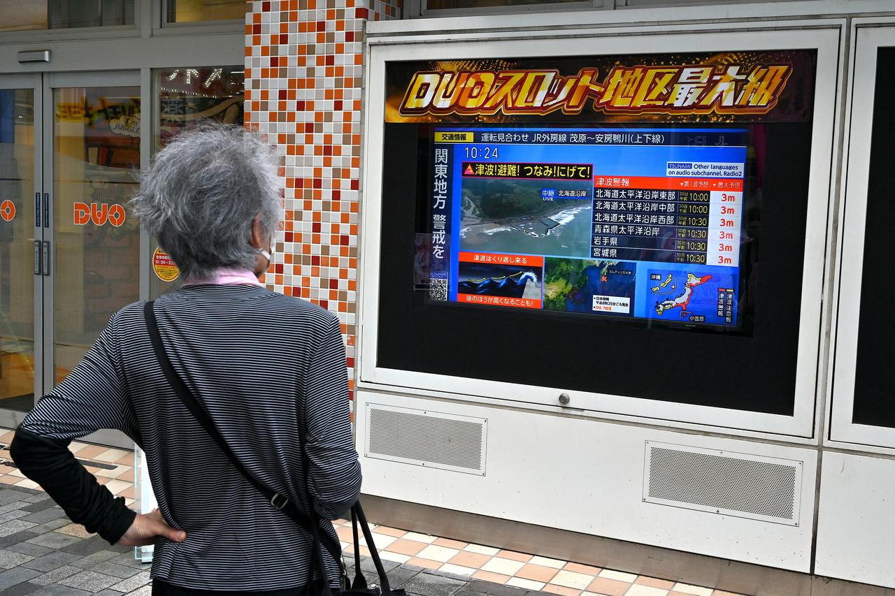 A woman is shown watching a TV broadcast, which displays a tsunami warning issued for a large part of Japan's coast. This warning came after a powerful 8.7 magnitude earthquake hit the sea near eastern Russia. (AFP Photo)