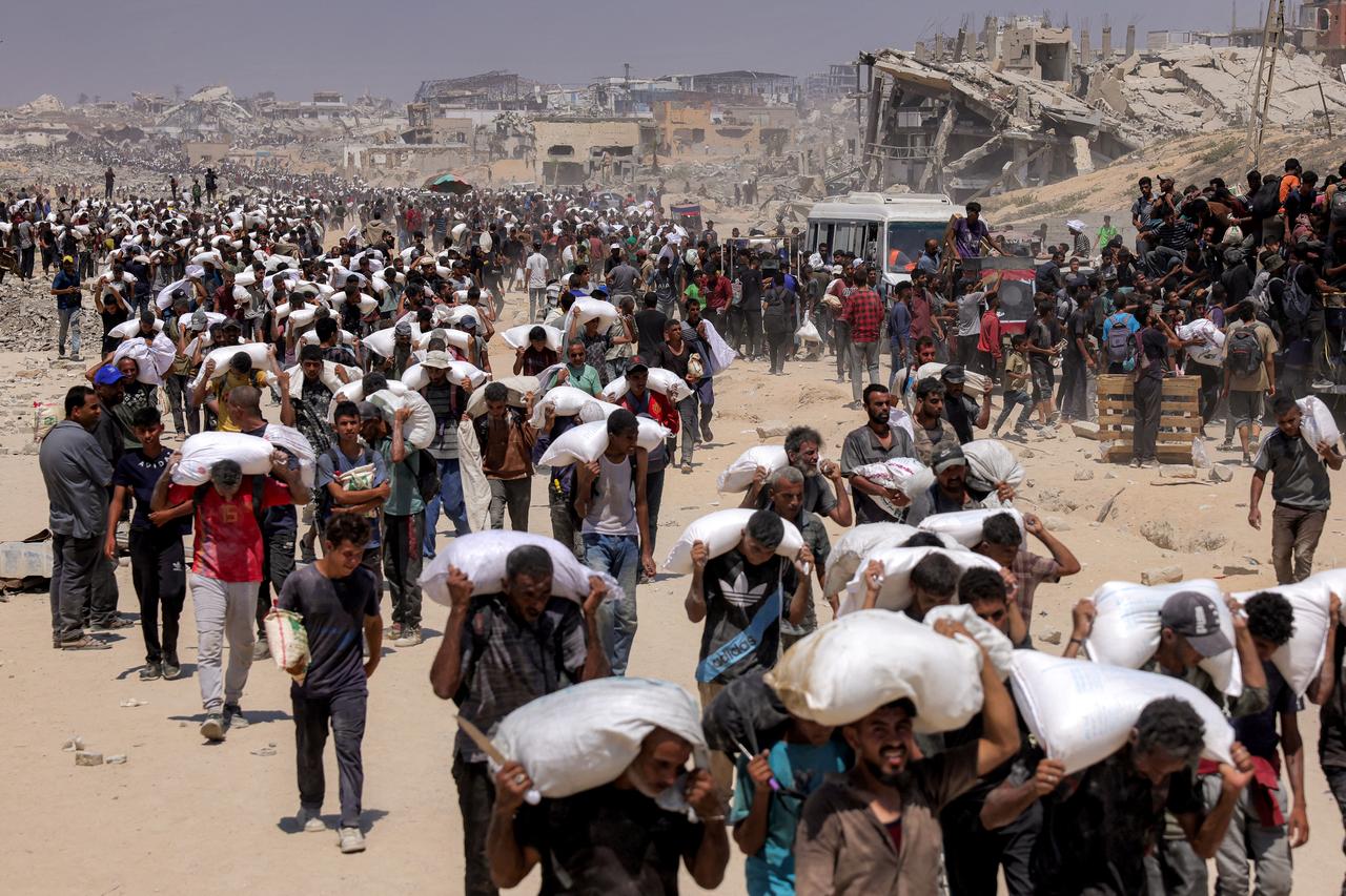 People walk with sacks of flour delivered after trucks carrying humanitarian aid entered northern Gaza on July 27, 2025. (AFP Photo)