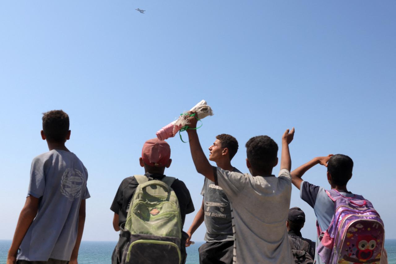 Children and youths gather as a C-130 Hercules military transport aircraft flies over during an aid drop on the northern Gaza Strip on July 27, 2025. (AFP Photo)
