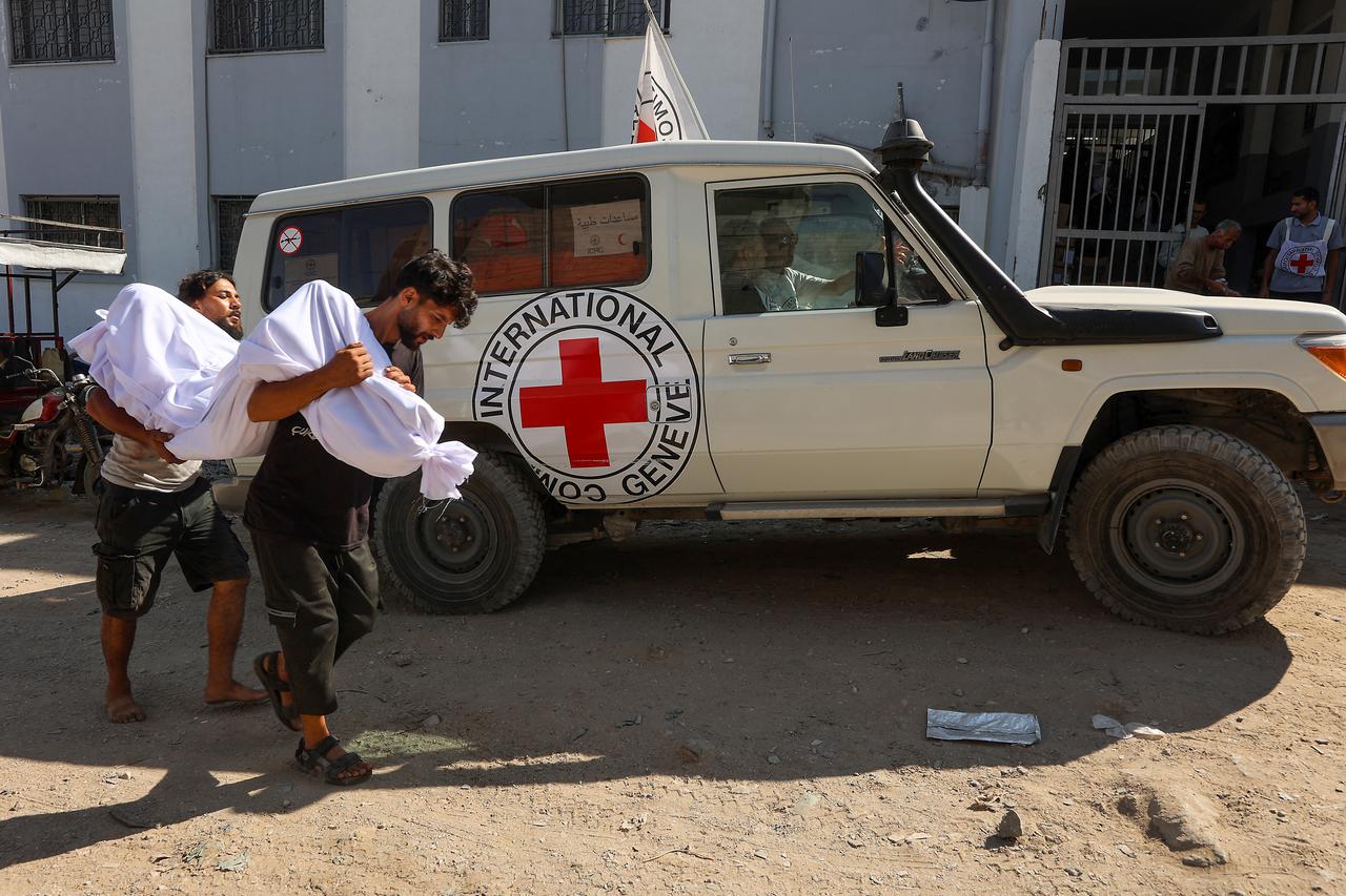 Palestinian men carry the body of a person reportedly killed while waiting for aid delivery, as they walk past an International Red Cross vehicle outside al-Shifa hospital in Gaza City, on July 3, 2025. (AFP Photo)